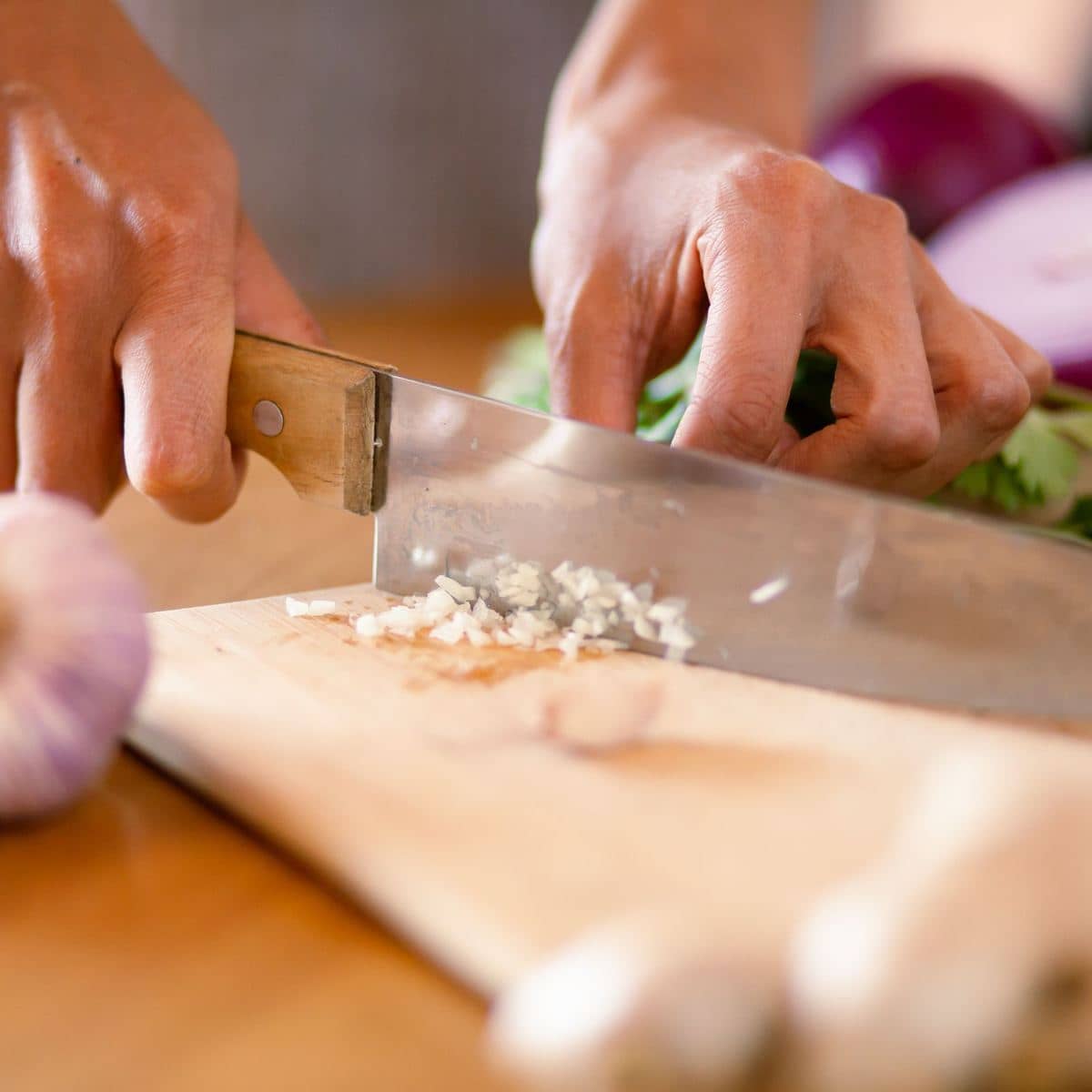 Hands chopping garlic on a wooden board while a simple meal is prepared Hands chopping garlic on a wooden board while a simple meal is prepared