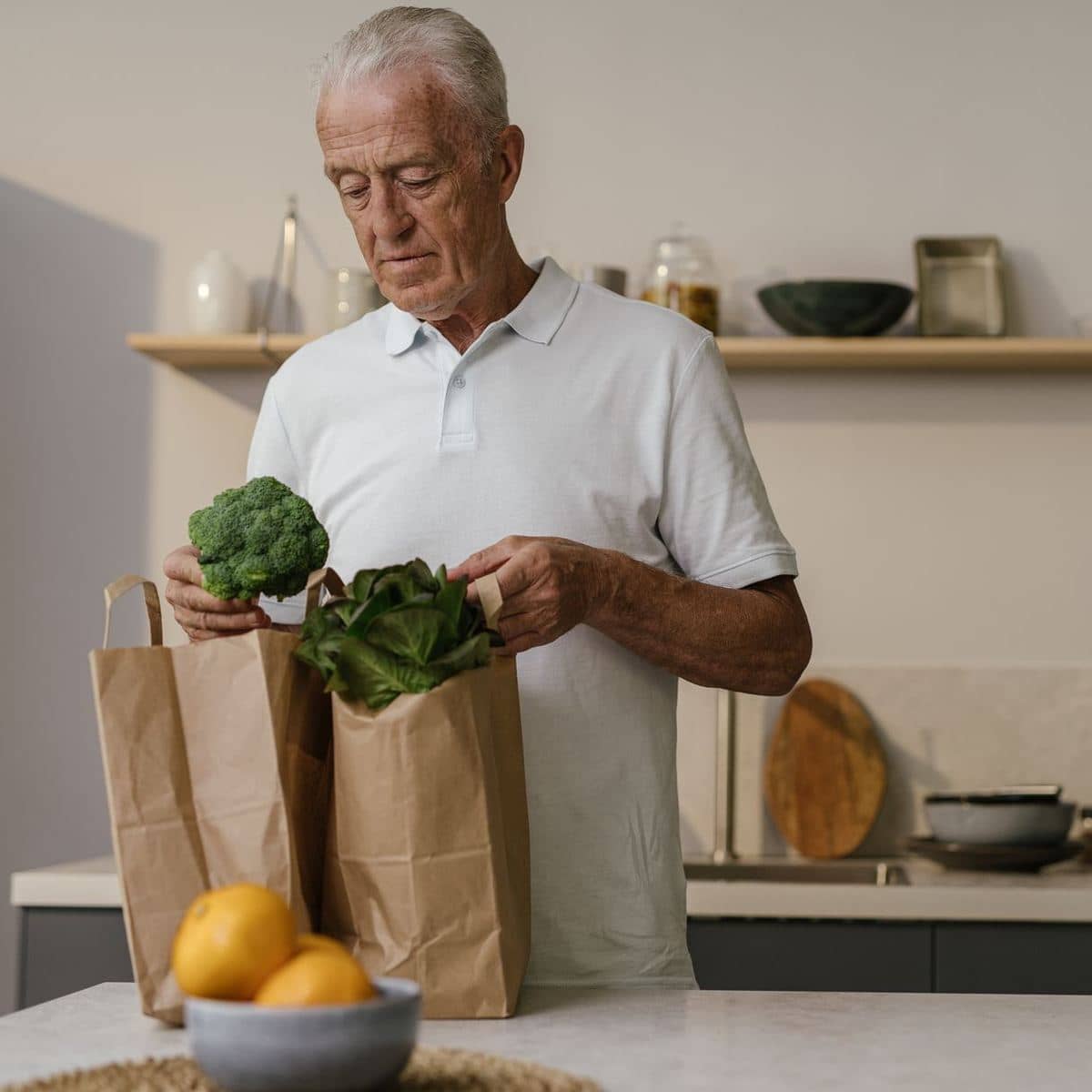 An older man unpacking a paper bag of groceries in his kitchen An older man unpacking a paper bag of groceries in his kitchen