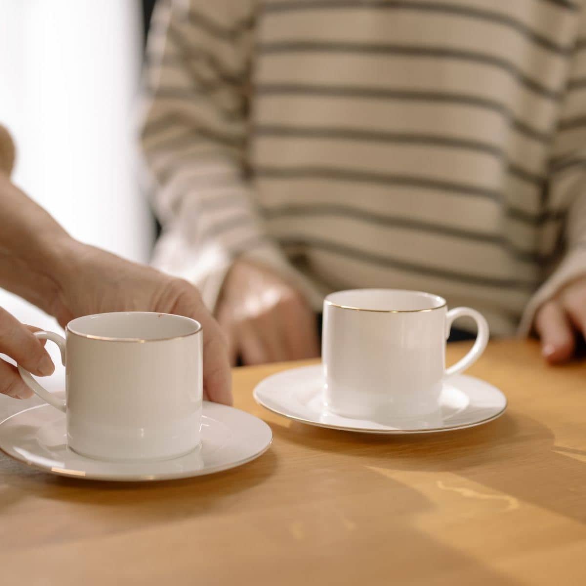 Two cups of tea on a wooden table, one being passed across Two cups of tea on a wooden table, one being passed across