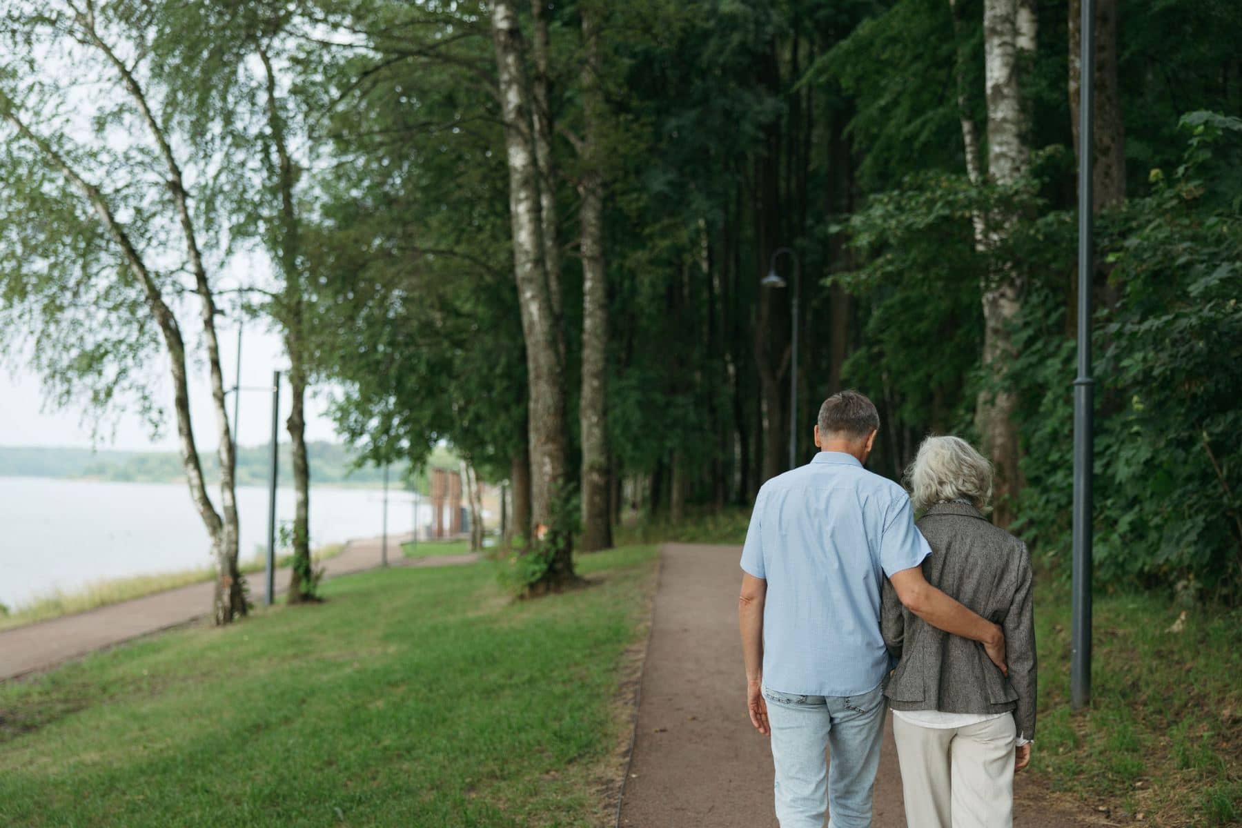 Two people walking arm in arm along a tree-lined path beside the water Two people walking arm in arm along a tree-lined path beside the water