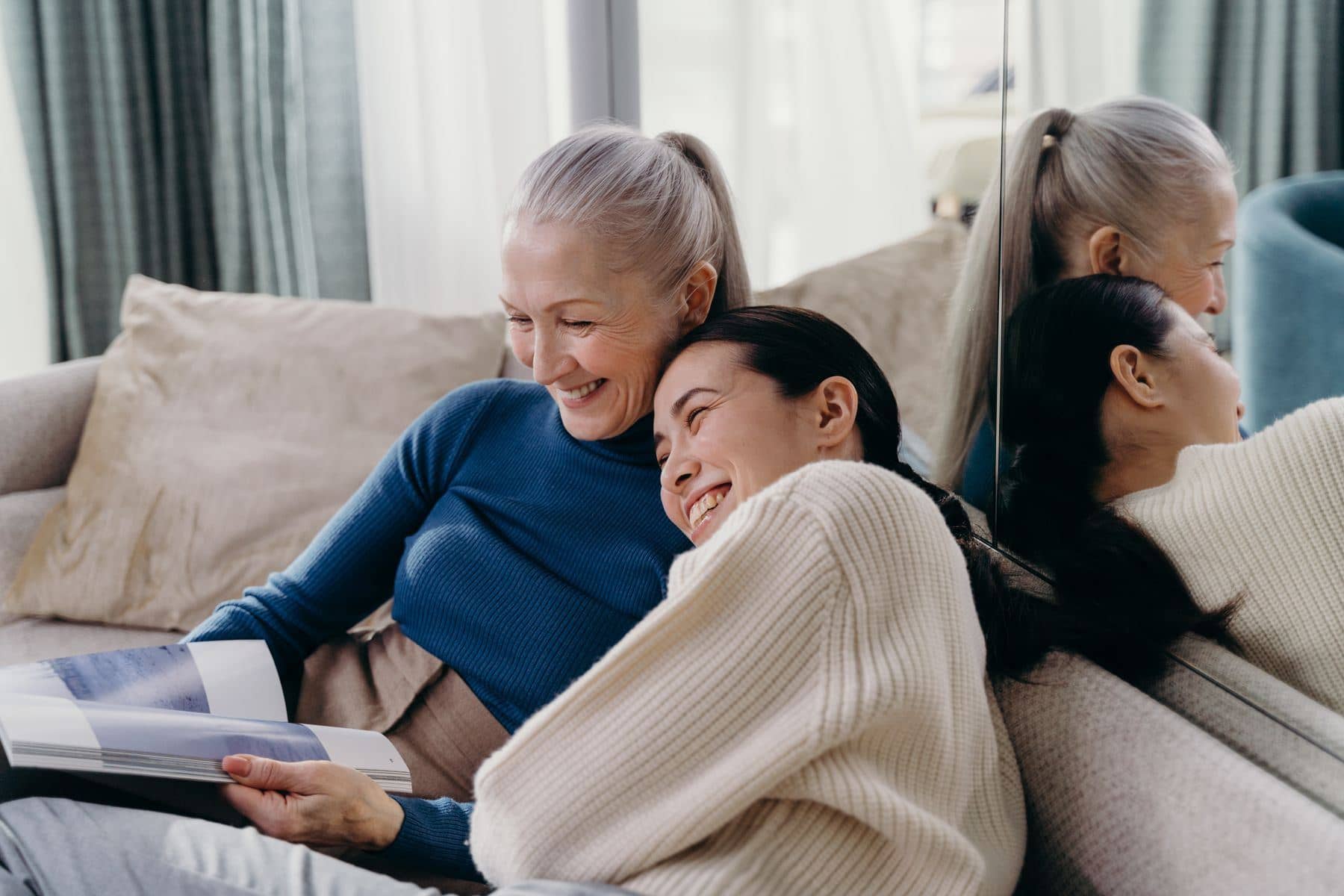 Two women laughing together on a sofa at home in the afternoon light Two women laughing together on a sofa at home in the afternoon light