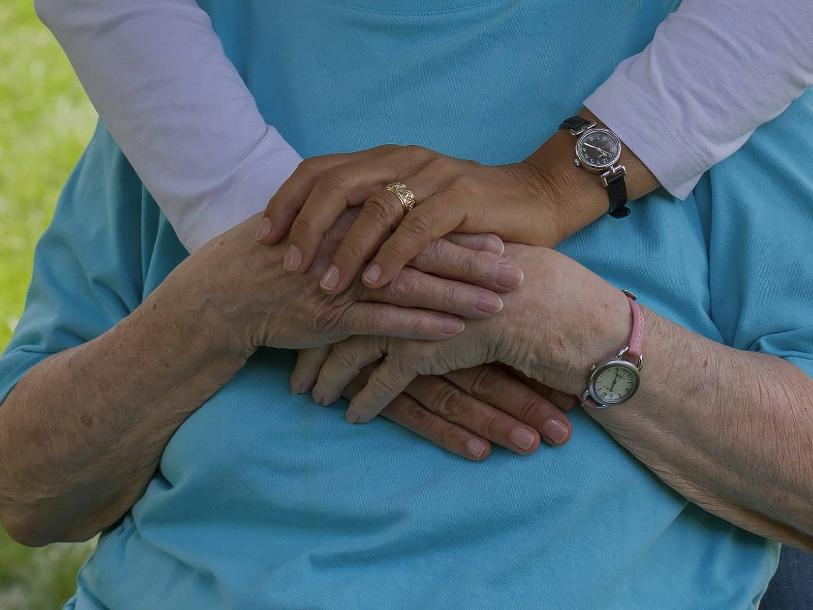 One person's hands resting gently over an older person's hands One person's hands resting gently over an older person's hands